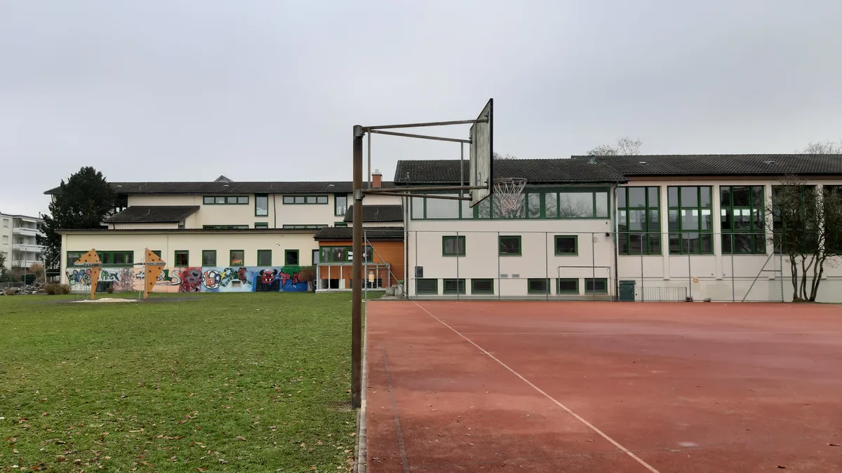 Weil die Schüler während der rund zweijährigen Bauzeit klassenweise auf die übrigen Schulhäuser verteilt werden, muss auf dem Schulareal kein Provisorium aufgestellt werden. (Archiv) Aussenansicht eines Schulhauses mit Sportplatz.